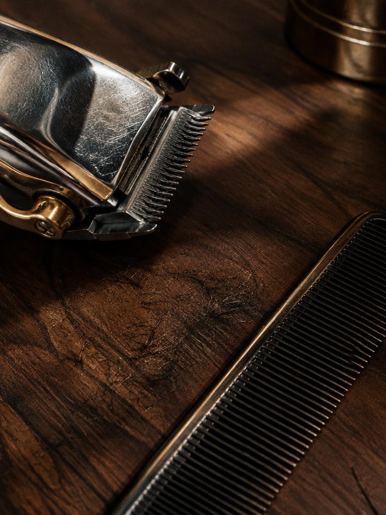 Close-up of a chrome clipper blade and fade comb on walnut